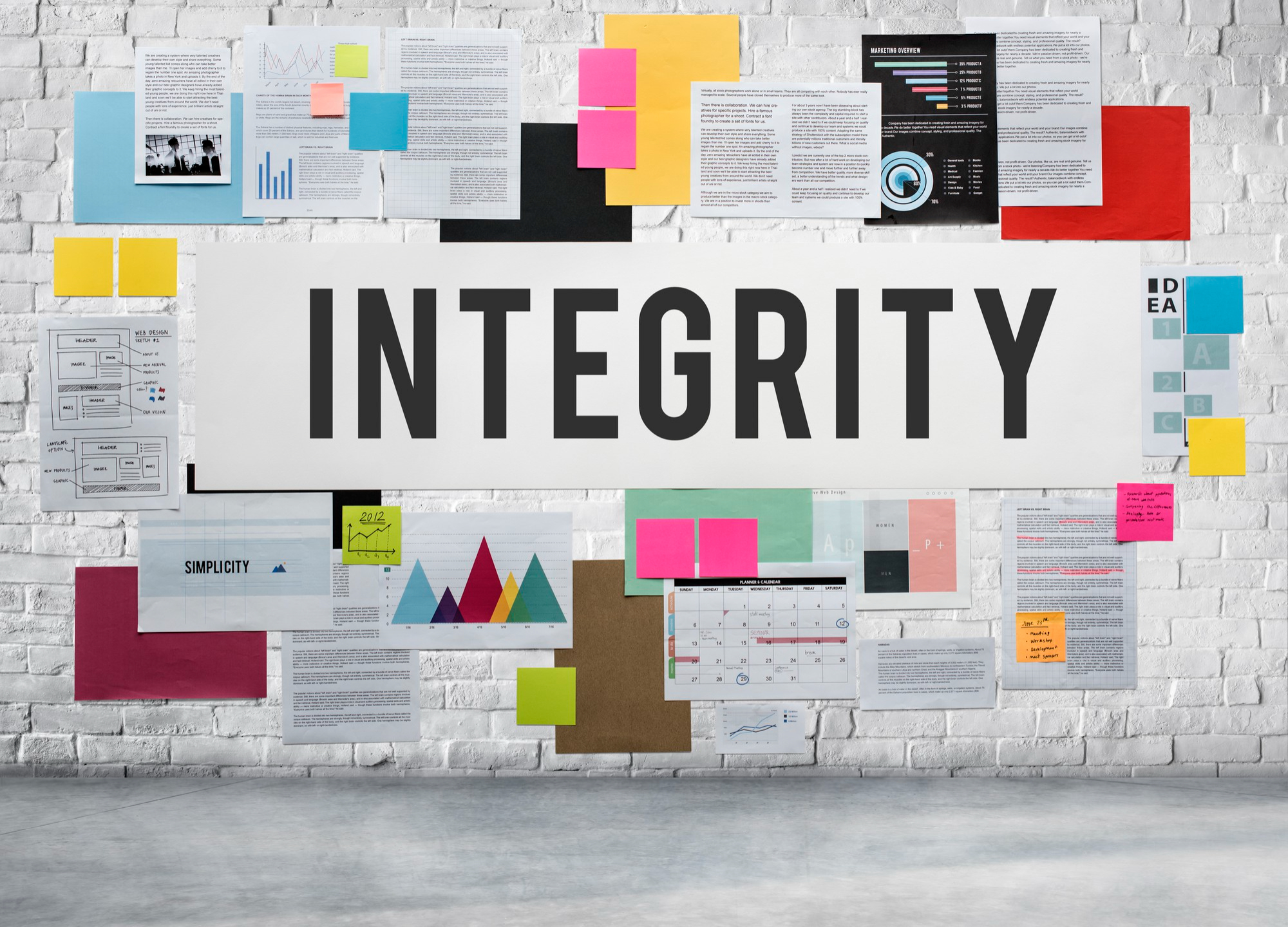 Notes and papers pasted on a brick wall with the word "Integrity" highlighted