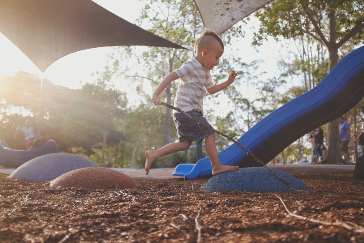 Young Boy with a Mohawk and a Stick Running By a Slide at Sunset