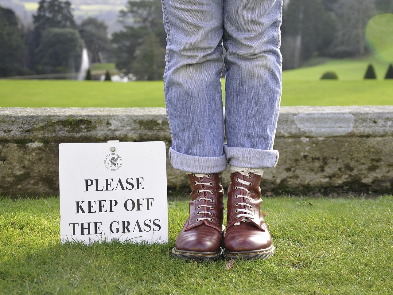 Man Standing on Grass next to "Please Keep Off the Grass" Sign