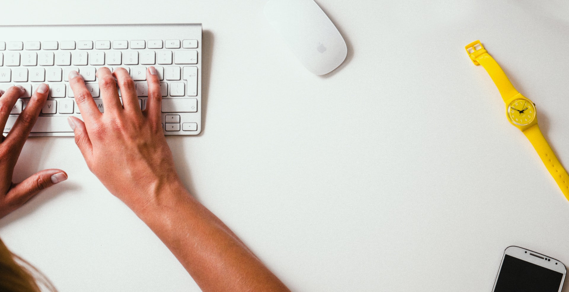 A keyboard, a mouse and a wristwatch placed on a white surface