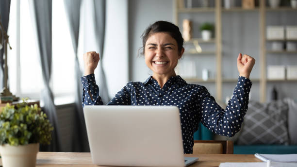 A woman exclaiming happily while sitting in front of a laptop