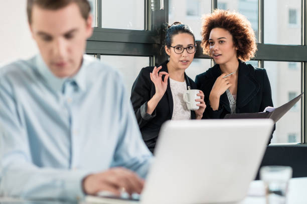 Two women talking about a guy who's working on a laptop