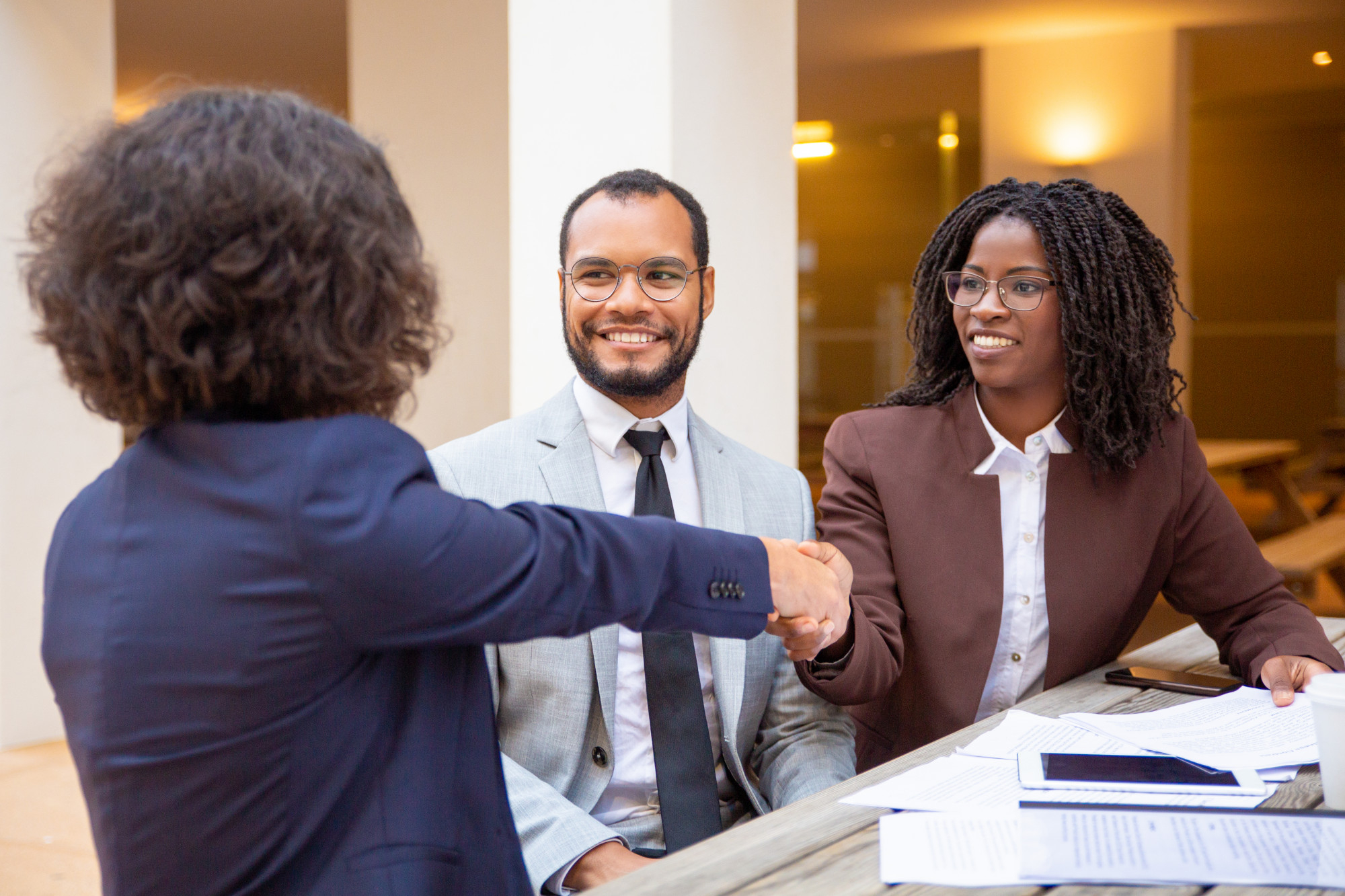 Two women jubilantly shaking hands and a man smiling at the woman on the left